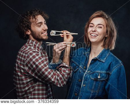 Young Couple In Love Eat Sushi On Bruderschaft, Enjoys And Having Fun Together. Studio Photo
