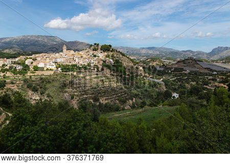 Sunny Panorama View Of The Hills Of Polop De Marina With Church And Castell Over Green Forest At The
