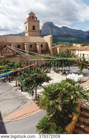 Main Square With Colorful Flags At The Church Of Polop De Marina With Rocky Mountainrange, Costa Bla