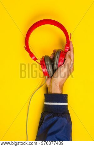 Hand Holding Red Headphones On Yellow Background. Music Concept