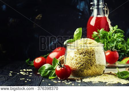 Italian Uncooked Pasta Riso Or Orzo In A Glass Jar, Tomatoes And Green Basil, Black Background, Sele