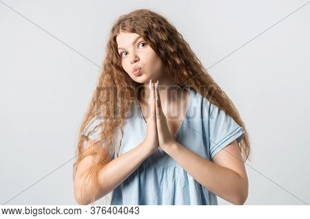 Please, Help Me. Emotive Pleased European Girl With Curly Long Hair, Keeps Hands In Praying Gesture,