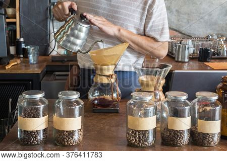 Barista Holding Drip Pot And Pouring Water Onto Ground Coffee Beans In The Paper Filter For Brewing 