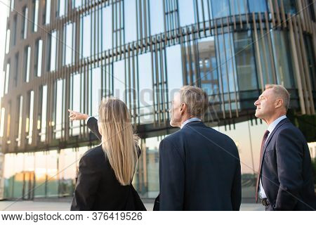 Businesspeople In Suits Pointing And Looking At Office Building, Discussing Real Property. Back View