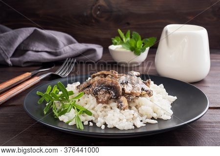 Risotto With Mushrooms On A Black Plate. Boiled White Rice With Champignons In Cream Sauce. Dark Woo