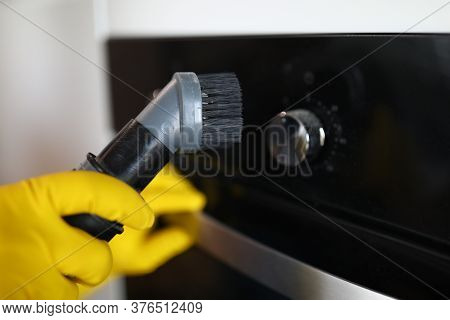 Close-up Of Persons Hand Cleaning Cookstove Display With Nozzle Of Grey Vacuum Cleaner. Male In Prot