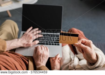 Cropped View Of Senior Man Using Aptop With Blank Screen Near Wife Holding Credit Card, Top View