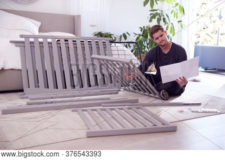 Confused Father To Be Looking At Instructions For Self Assembly Baby Cot