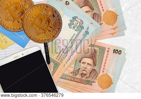100 Ukrainian Hryvnias Bills And Golden Bitcoins With Smartphone And Credit Cards. Cryptocurrency In