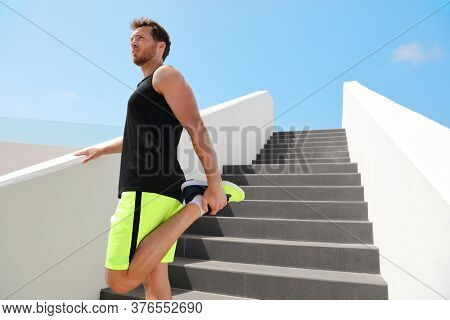 Leg muscles stretch fit man runner getting ready to run stretching legs warm-up quad stretches exercises on outdoor stairs for cardio HIIT summer workout.