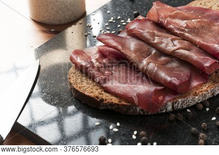 Slice Of Wholemeal Bread With Bresaola (dried Beef) On A Black Granite Cutting Board. Bresaola Is A 