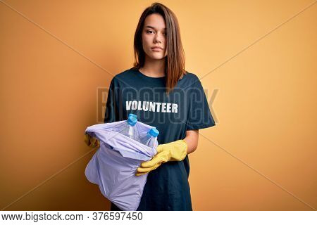 Beautiful volunteer girl caring environment doing volunteering holding bag with rubish bottles with a confident expression on smart face thinking serious