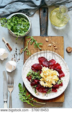 Scramble Of Eggs With Carpaccio Of Baked Beets With Walnuts, Aromatic Herbs And Arugula On A Plate. 
