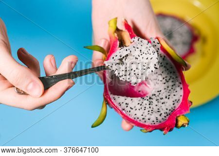 Half-cut Pitaya Fruit. Red Dragon Fruit In The Girls Hand. A Girl Eats A Tropical Fruit With A Spoon