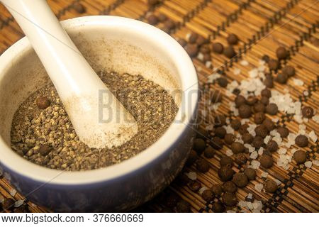 Ground Black In A Ceramic Mortar And Black And Coarse Salt Scattered On A Reed Mat. Close Up.