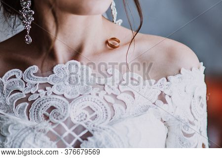Bride In A Wedding Dress And Long Earrings With A Wedding Ring On The Collarbone