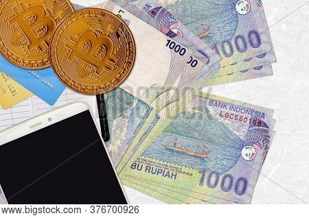 1000 Indonesian Rupiah Bills And Golden Bitcoins With Smartphone And Credit Cards. Cryptocurrency In