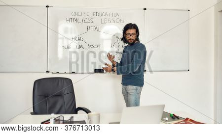 Code Academy Online. Young Serious Bearded Male Teacher Wearing Glasses Pointing At Whiteboard And T