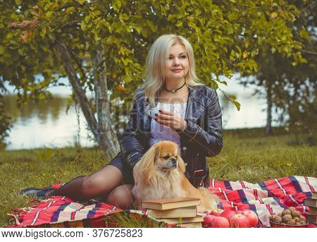 Middle Age Stylish Blonde Hair Pretty Woman Dressed In Leather Black Jacket  In Autumn Garden With P