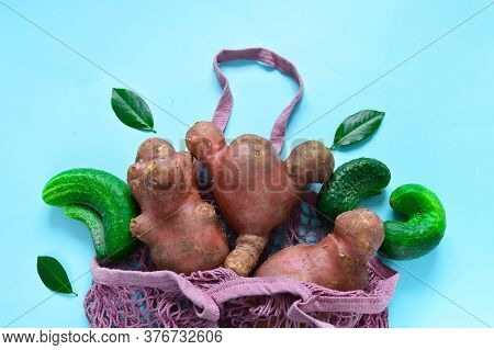 Fresh Ugly Cucumbers And Potatoes In A String Bag On A Blue Background. Trendy Ugly Vegetables. Impe