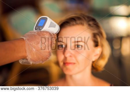 A Worker Measuring Temperature Of Woman Visitior Inside  Of The Cafe. Life During Coronavirus Time