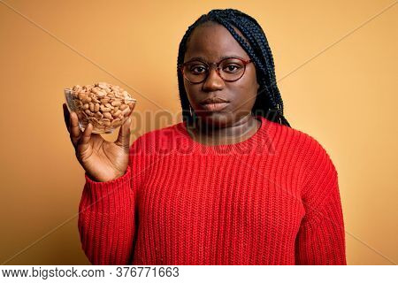 Young african american plus size woman with braids holding bowl with healthy peanuts with a confident expression on smart face thinking serious