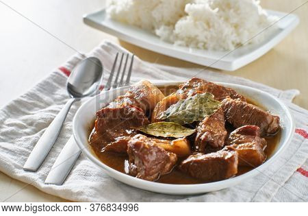 filipino pork adobo in bowl with rice in background