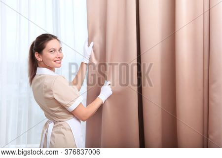 A Uniformed Maid Adjusts The Curtains In A Hotel Room. The Concept Of The Hotel Business. Cleaning I