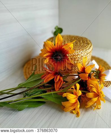 Golden Bicolor Rudbeckia Lies On A Wicker Straw Hat On A Light Wood Background. Selective Focus