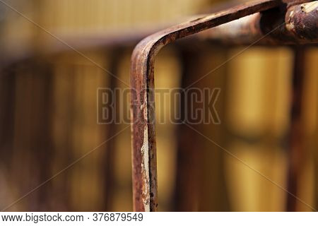 A Small Part Of A Rusty Ladder Hanging On A Yellow House Wall