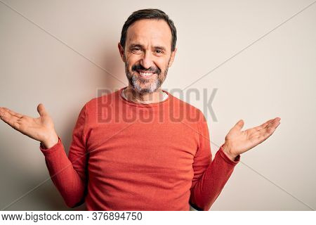 Middle age hoary man wearing casual orange sweater standing over isolated white background smiling showing both hands open palms, presenting and advertising comparison and balance