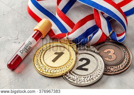Doping Test. Gold, Silver And Bronze Medal And Test Tube With Blood On A Gray Background
