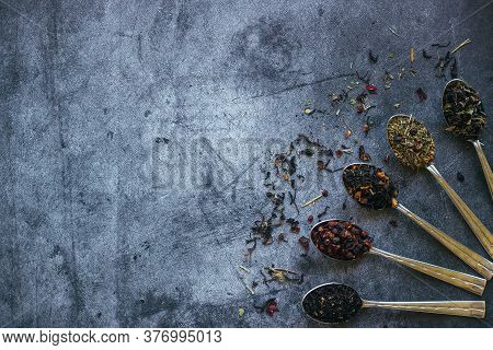 Various Types Of Herbal Tea In Spoons. Spoons With Dry Tea Leaves. Tea On A Concrete Background