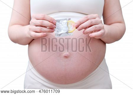 A Condom In The Hands Of A Pregnant Woman, A Studio Photo, Isolated On A White Background