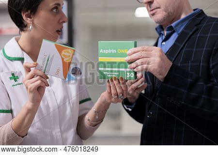 Pharmacy Assistant Recommending Vitamin And Aspirin To Client, Helping To Choose Anti Inflammatory P