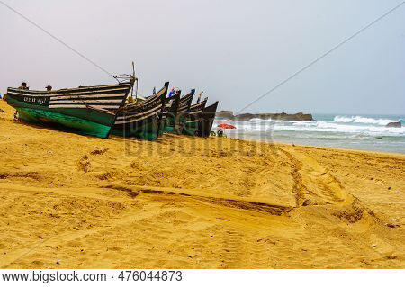 Oualidia, Morocco - April 08, 2023: View Of Wooden Boats On The Beach, With Locals, In The Village R