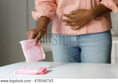 Classic Comfort Of Menstrual Pads. Black Woman Taking Sanitary Napkin From Table, Suffering From Men
