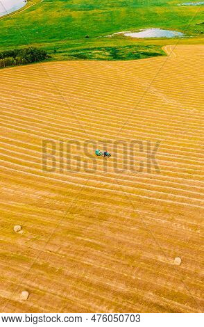 Aerial View Tractor Collects Dry Grass In Straw Bales In Wheat Field. Special Agricultural Equipment