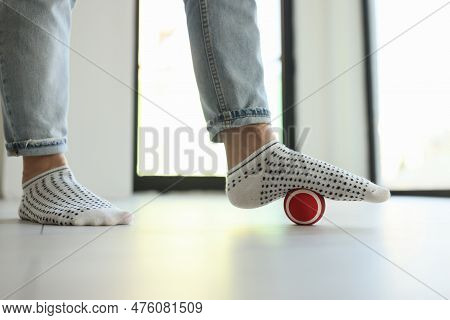Close-up Of Woman Massaging Foot With Ball To Eliminate Feet Tension. Female Person In Jeans And Soc
