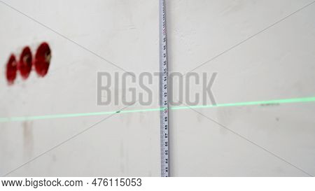 A Man Uses A Cross Laser Level And A Tape For Accurate Measurements On A Light Wall, Close-up. Measu