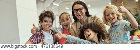 We Are The Best. Happy School Team Of Four Cute Little Pupils And Their Friendly Female Teacher Posi