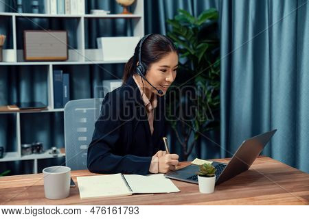 Asian Call Center With Headset And Microphone Working On Her Laptop. Female Operator Provide Excepti