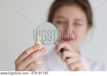 Young Woman Looks At Small Wooden Figurine In Hand Through Loupe. Female Person Examines Human Figur