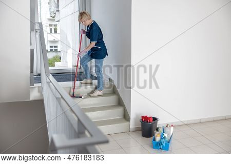 Cleaning Lady In Uniform With Mop And Rag Washes A Dusty Steps Of The House