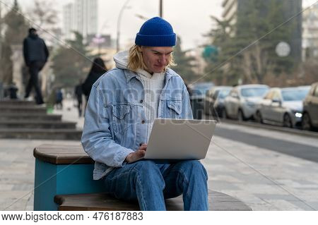 Smiling Millennial Guy Remote Worker Working Outside, Sitting On Bench Outdoors With Laptop Computer