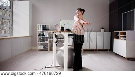 Woman Using Adjustable Height Standing Desk In Office For Good Posture