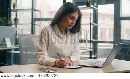 Multiracial Serious Businesswoman In Office Working With Laptop Writing Notes Indian Girl Arabian Et