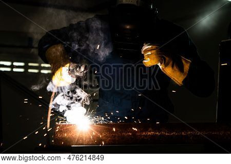 Metal Welder Working With Arc Welding Machine To Weld Steel At Factory While Wearing Safety Equipmen