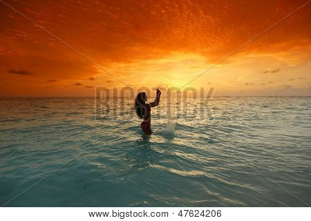 Vrolijke vrij jonge vrouw splashin in zee op zonsondergang