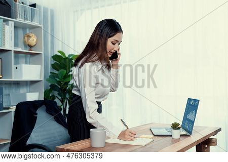 Young Enthusiastic Businesswoman Talking On Business Call And Writing Notes On Her Laptop As Multita